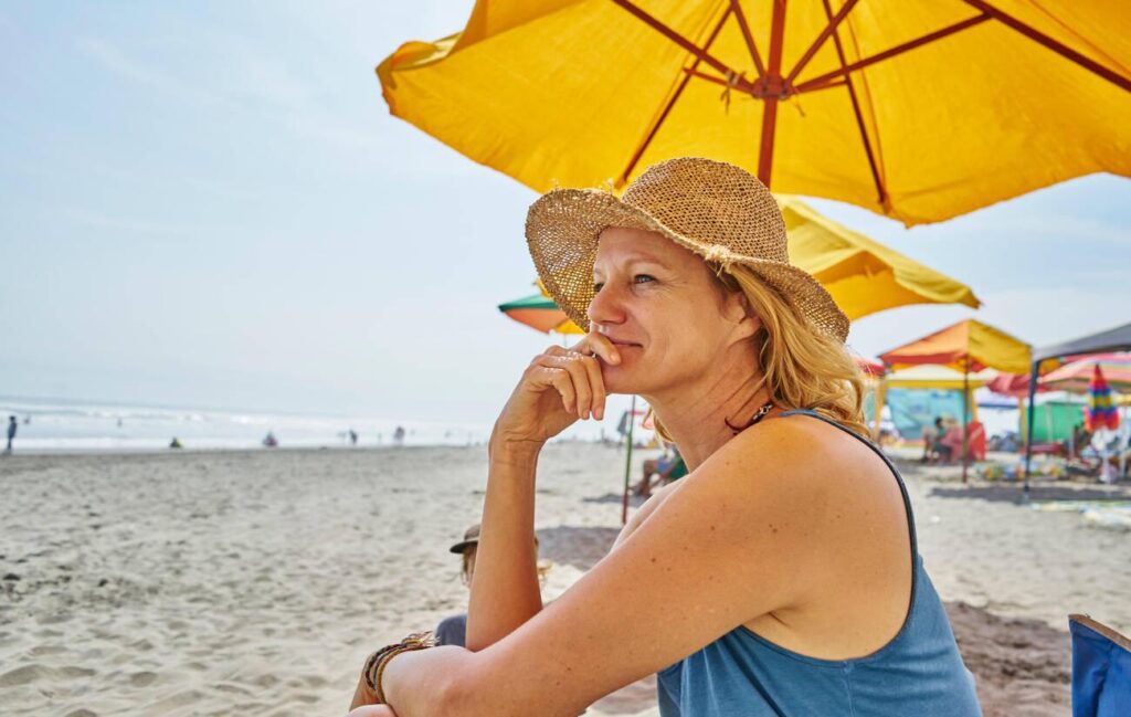 Female tourist sitting under beach umbrella